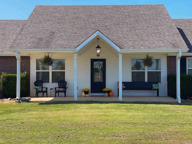 view of front of home featuring a front yard, brick siding, covered porch, and a shingled roof