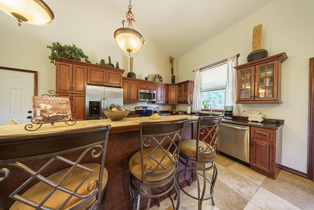 kitchen with light tile patterned floors, a breakfast bar, stainless steel appliances, hanging light fixtures, and dark stone counters