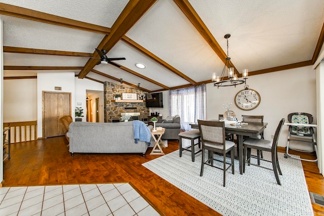 dining area with hardwood / wood-style floors, ceiling fan with notable chandelier, vaulted ceiling with beams, and a stone fireplace