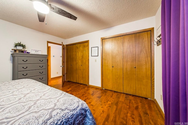 bedroom featuring dark wood-type flooring, two closets, ceiling fan, and a textured ceiling