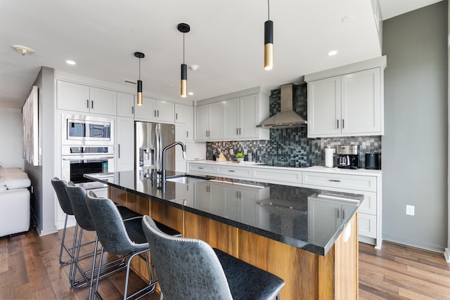 kitchen featuring white cabinets, appliances with stainless steel finishes, sink, wall chimney range hood, and a kitchen island with sink