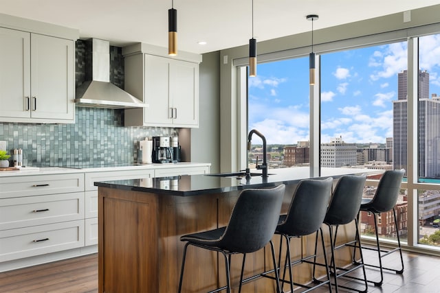 kitchen featuring a center island with sink, hanging light fixtures, a wealth of natural light, and wall chimney range hood