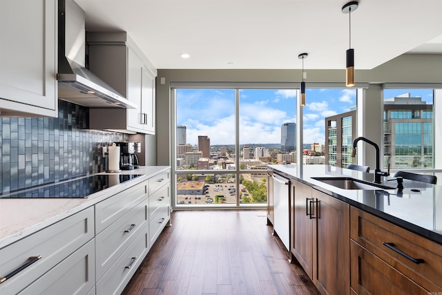 kitchen featuring wall chimney exhaust hood, pendant lighting, sink, black electric stovetop, and white cabinets