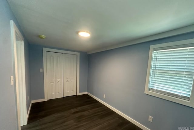 unfurnished bedroom with multiple windows, dark wood-type flooring, and a closet