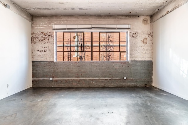 spare room featuring brick wall and concrete flooring