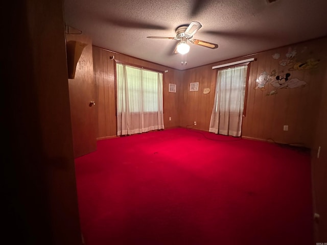 carpeted spare room featuring wood walls, ceiling fan, and a textured ceiling