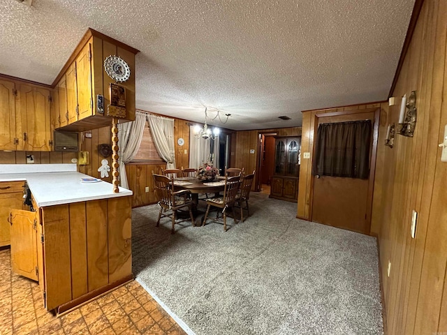 kitchen featuring a textured ceiling, light colored carpet, kitchen peninsula, and wood walls