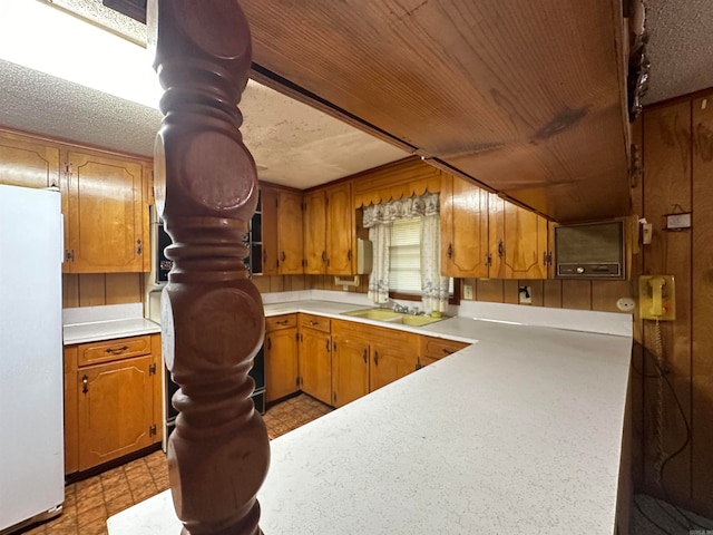 kitchen featuring a textured ceiling, sink, white refrigerator, and wooden walls