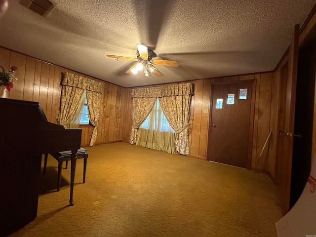 interior space with wood walls, ceiling fan, carpet, and a textured ceiling