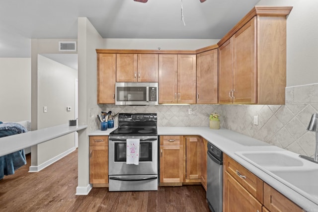 kitchen with dark wood-type flooring, stainless steel appliances, sink, decorative backsplash, and ceiling fan