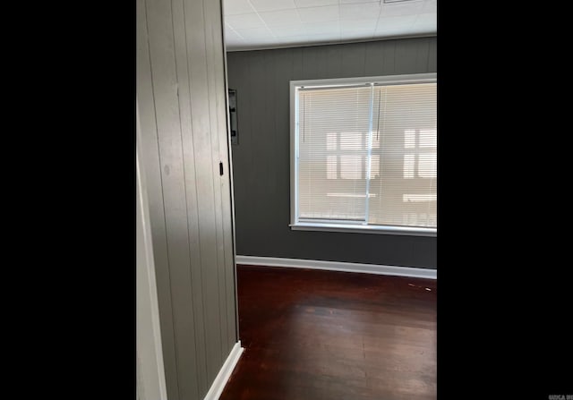 unfurnished room featuring wooden walls and dark wood-type flooring