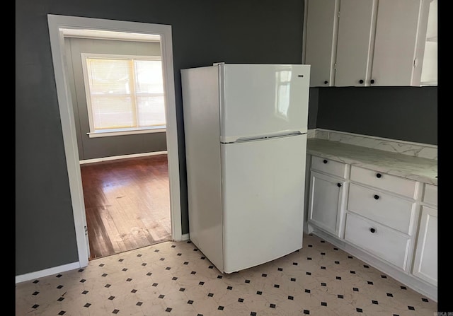 kitchen with white cabinetry, light hardwood / wood-style flooring, light stone countertops, and white refrigerator