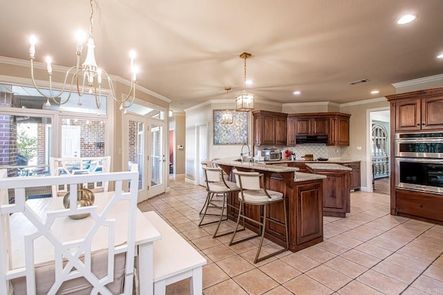 kitchen featuring pendant lighting, stainless steel double oven, light tile patterned floors, an inviting chandelier, and a center island with sink