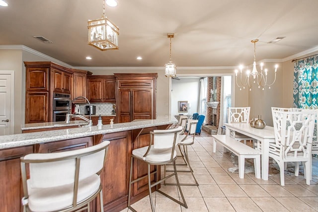 kitchen featuring an inviting chandelier, a breakfast bar, ornamental molding, a brick fireplace, and light stone counters