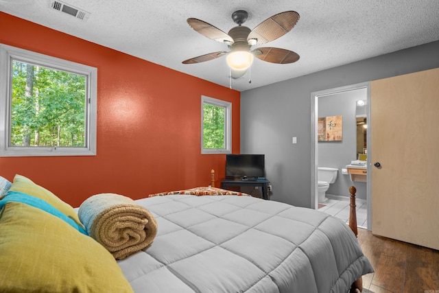 bedroom with multiple windows, ceiling fan, hardwood / wood-style floors, and ensuite bathroom