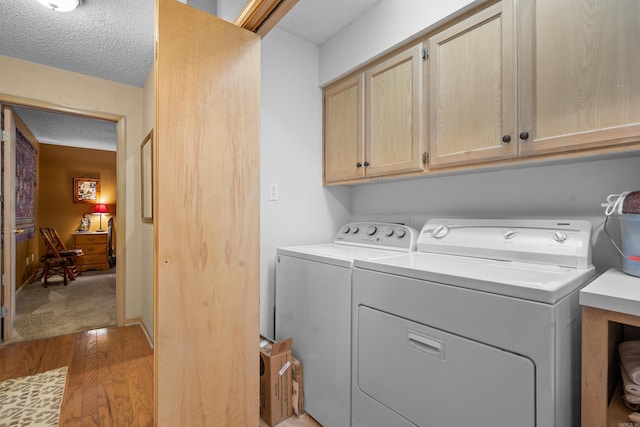 laundry area with a textured ceiling, cabinets, independent washer and dryer, and light wood-type flooring