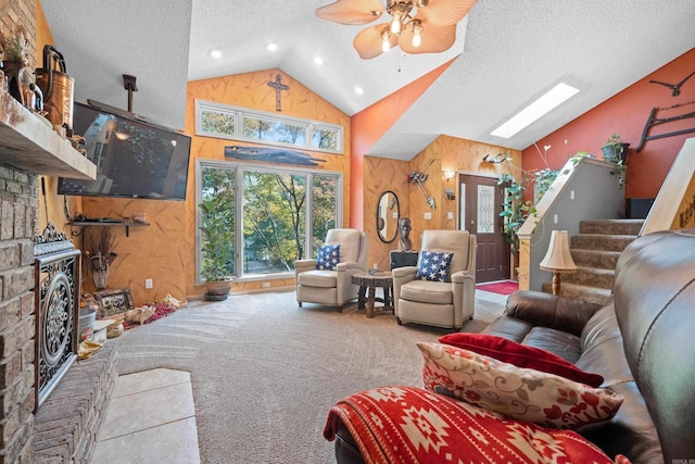 living room with high vaulted ceiling, a textured ceiling, a skylight, ceiling fan, and a stone fireplace