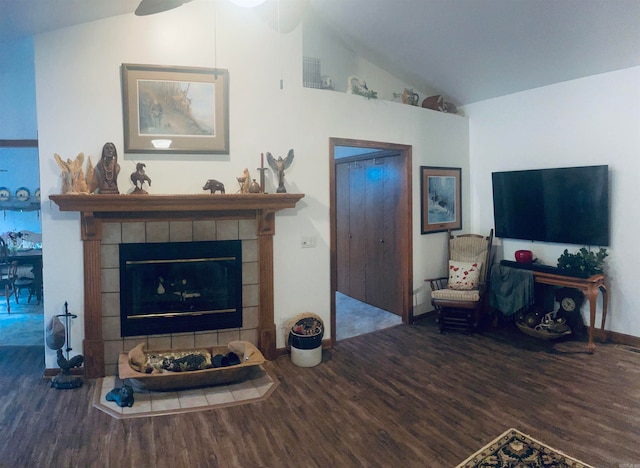 living room with wood-type flooring, vaulted ceiling, ceiling fan, and a tiled fireplace