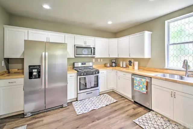 kitchen with light wood-type flooring, light countertops, appliances with stainless steel finishes, white cabinetry, and a sink