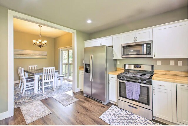 kitchen featuring white cabinetry, stainless steel appliances, wood counters, an inviting chandelier, and hanging light fixtures