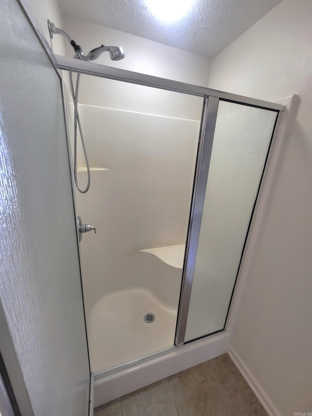 bathroom with a textured ceiling, an enclosed shower, and tile patterned flooring