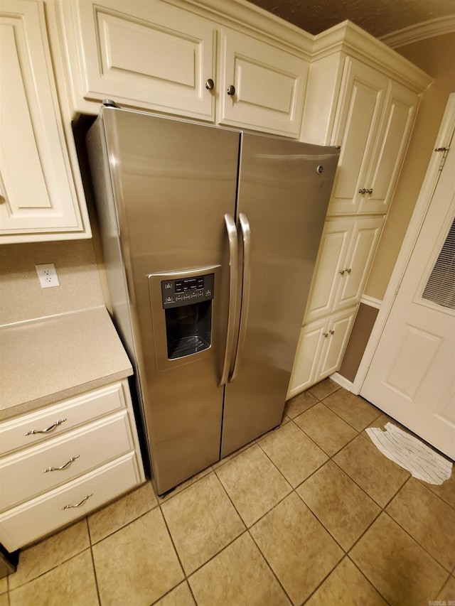 kitchen with stainless steel refrigerator with ice dispenser, ornamental molding, light tile patterned floors, and cream cabinetry