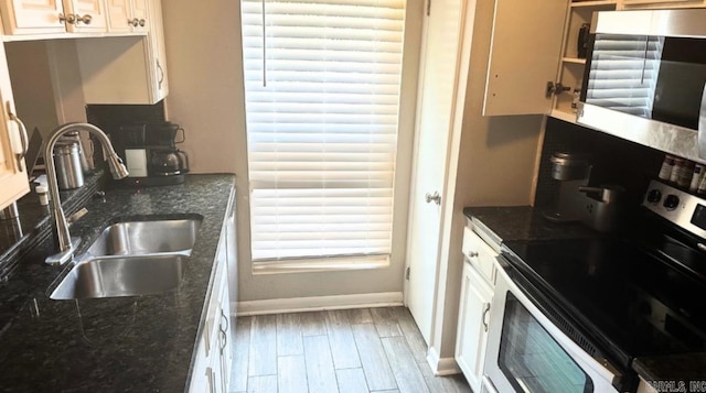 kitchen with stainless steel appliances, sink, white cabinetry, hardwood / wood-style flooring, and dark stone countertops