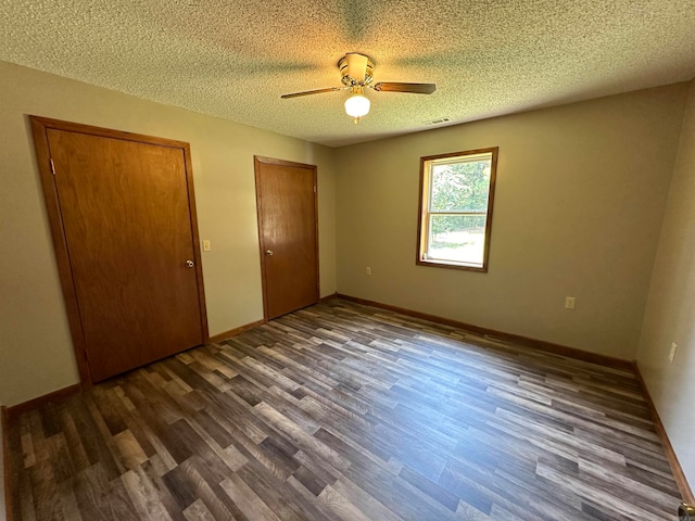 unfurnished bedroom with ceiling fan, dark wood-type flooring, a textured ceiling, and multiple closets