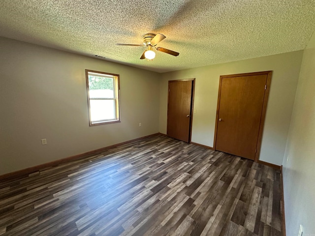 unfurnished bedroom with a textured ceiling, ceiling fan, dark wood-type flooring, and two closets