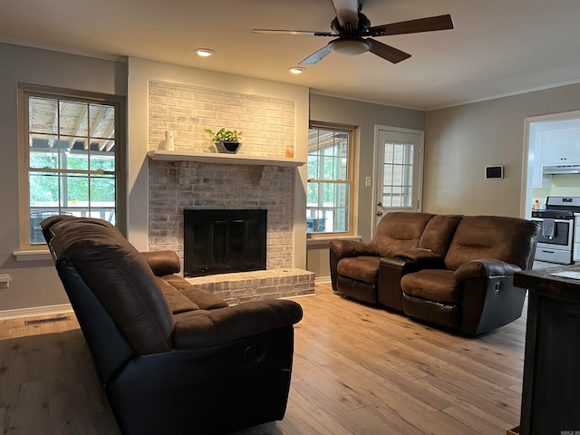 living room with crown molding, a brick fireplace, hardwood / wood-style floors, and ceiling fan