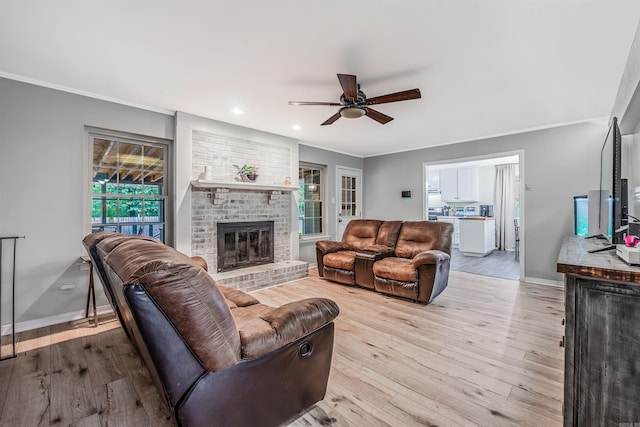 living room featuring ceiling fan, ornamental molding, a brick fireplace, and light hardwood / wood-style flooring