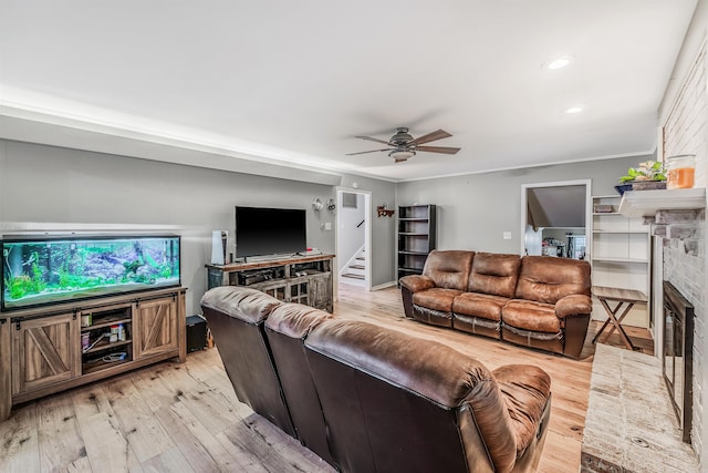 living room with crown molding, a brick fireplace, light hardwood / wood-style flooring, and ceiling fan