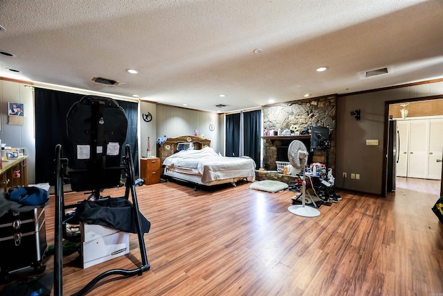 bedroom with a textured ceiling, wood walls, ornamental molding, and hardwood / wood-style floors