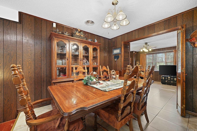 dining area featuring light tile patterned floors, ceiling fan with notable chandelier, a textured ceiling, wooden walls, and visible vents