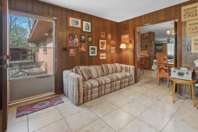 living room with a ceiling fan, wooden walls, and light tile patterned floors