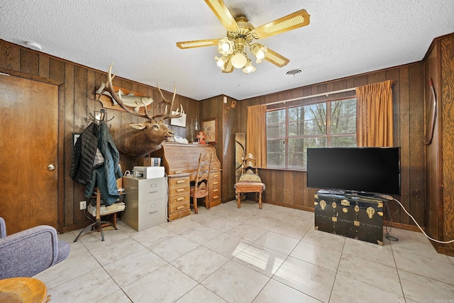 office with wood walls, light tile patterned floors, a textured ceiling, visible vents, and a ceiling fan