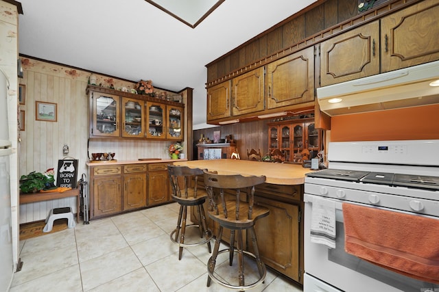 kitchen with light countertops, glass insert cabinets, under cabinet range hood, light tile patterned floors, and white range with gas stovetop