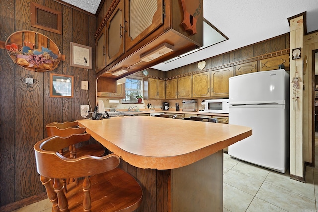 kitchen with light tile patterned floors, light countertops, wooden walls, and white appliances