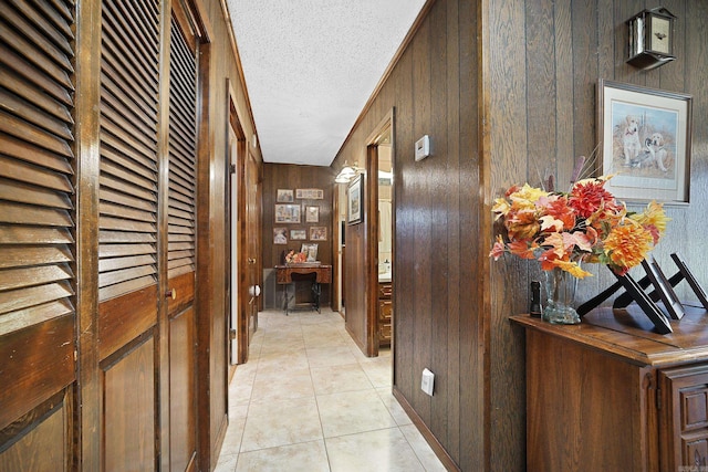 corridor featuring light tile patterned floors, wood walls, and a textured ceiling