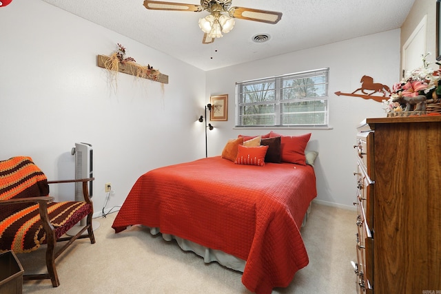 bedroom featuring a textured ceiling, baseboards, light colored carpet, visible vents, and ceiling fan
