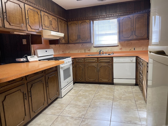 kitchen featuring light countertops, a sink, under cabinet range hood, light tile patterned floors, and white appliances