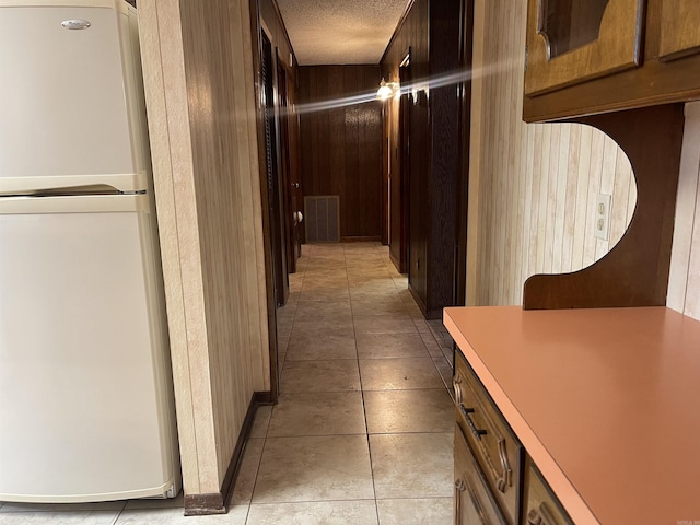 hall with a textured ceiling, visible vents, wooden walls, and light tile patterned floors