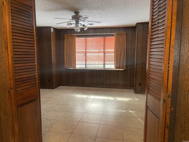 unfurnished room with a ceiling fan, light tile patterned floors, wood walls, and a textured ceiling