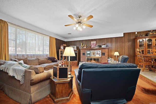 living area with a ceiling fan, wood walls, a fireplace, and a textured ceiling