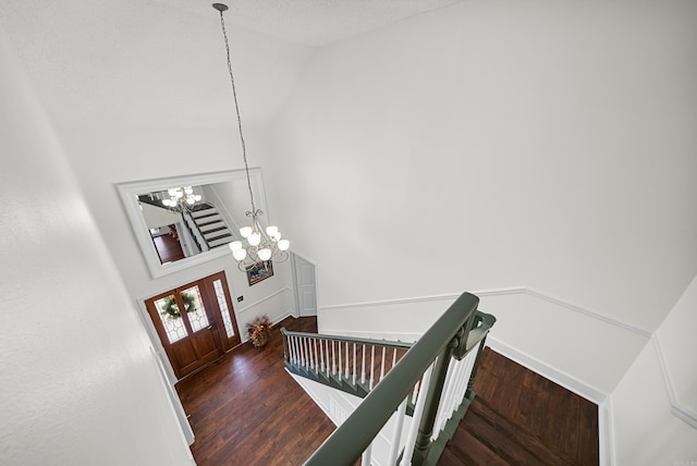 stairs with high vaulted ceiling, wood-type flooring, an inviting chandelier, and a textured ceiling