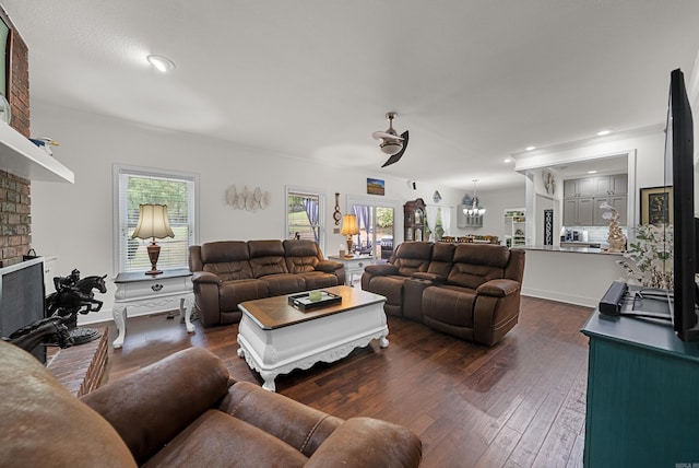 living room featuring crown molding, dark hardwood / wood-style floors, ceiling fan with notable chandelier, and a brick fireplace