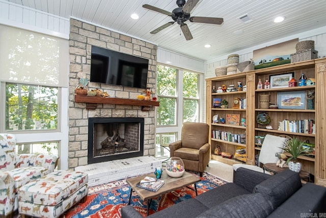 living room featuring ceiling fan, a stone fireplace, and wooden ceiling