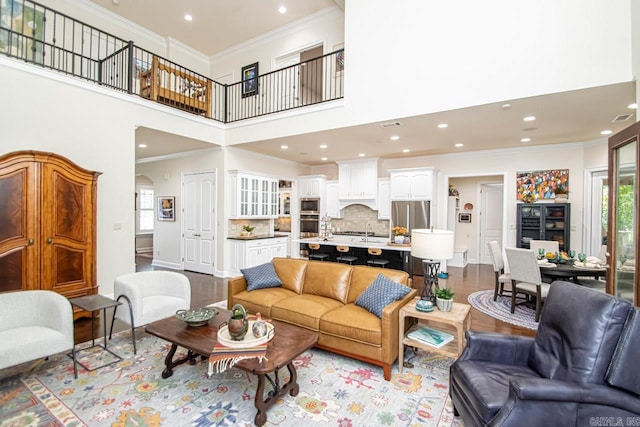 living room with ornamental molding, a towering ceiling, and light hardwood / wood-style flooring