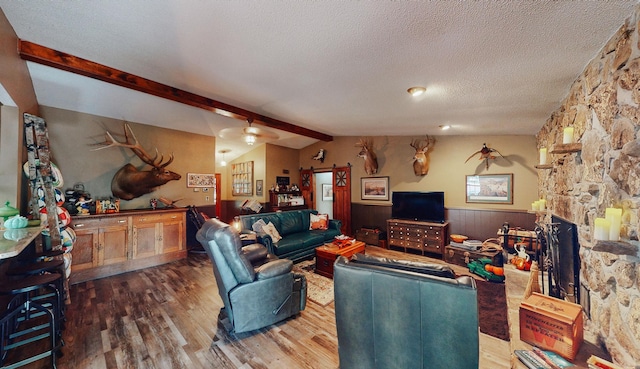 living room with a textured ceiling, dark wood-type flooring, a stone fireplace, wooden walls, and lofted ceiling with beams