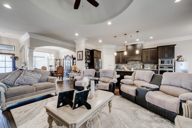 living room with ceiling fan with notable chandelier, light hardwood / wood-style floors, ornamental molding, and ornate columns